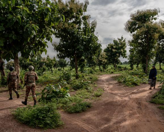 A civilian passes by soldiers on a foot patrol around their base, in Banikoara, Benin, on August 28th, 2023. Credit : Adrienne Surprenant/ MYOP for the Wall Street Journal